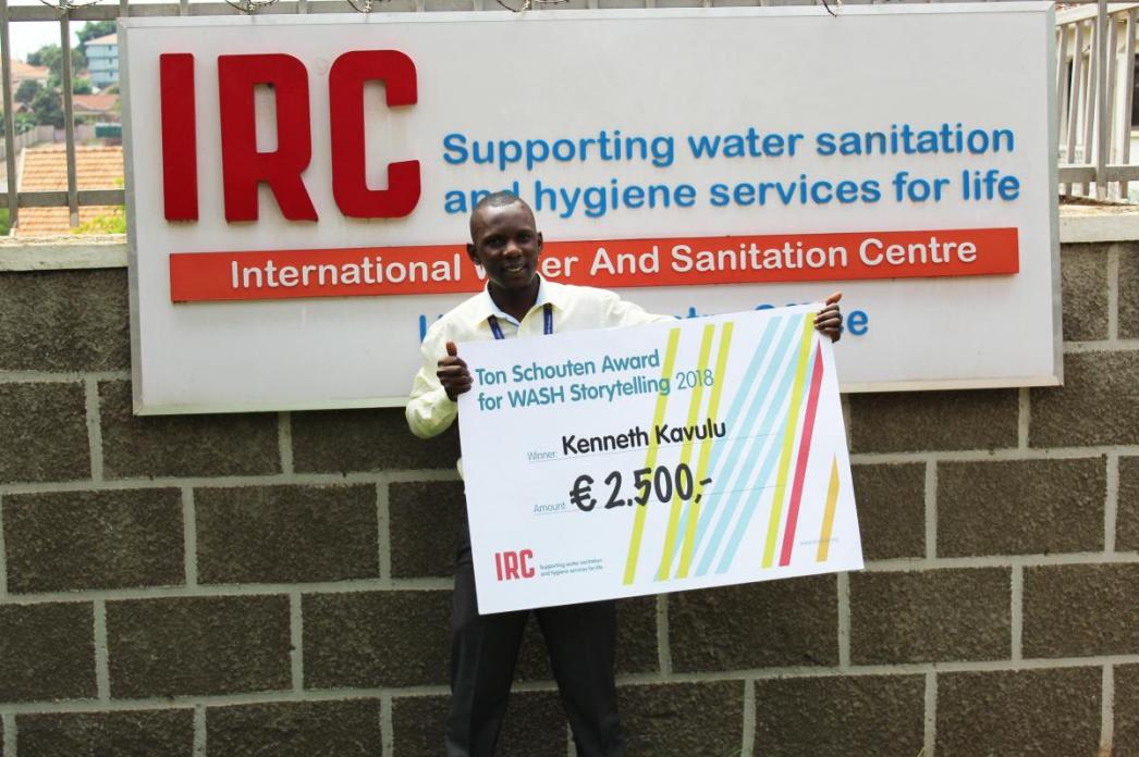 Kenneth Kavulu in front of IRC Uganda's office with a cheque announcing his 2500 euro cash award
