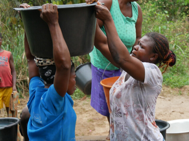 Woman helps other woman lifting her water bucket in Agravi community Ghana