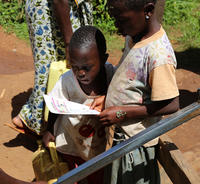 Children study a leaflet telling them how to report a fault at their water point. Karambi sub-county, Kabarole, Uganda.